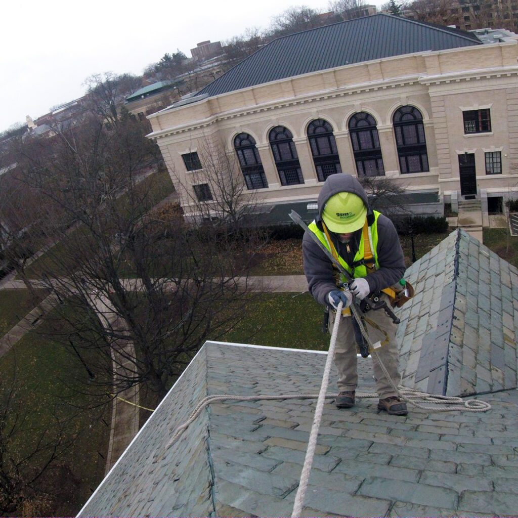 man high on rooftop straped in for safety