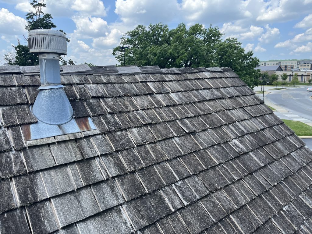 Aged cedar shake roof with vent and weathered appearance on a commercial building, prior to GSM Roofing restoration.