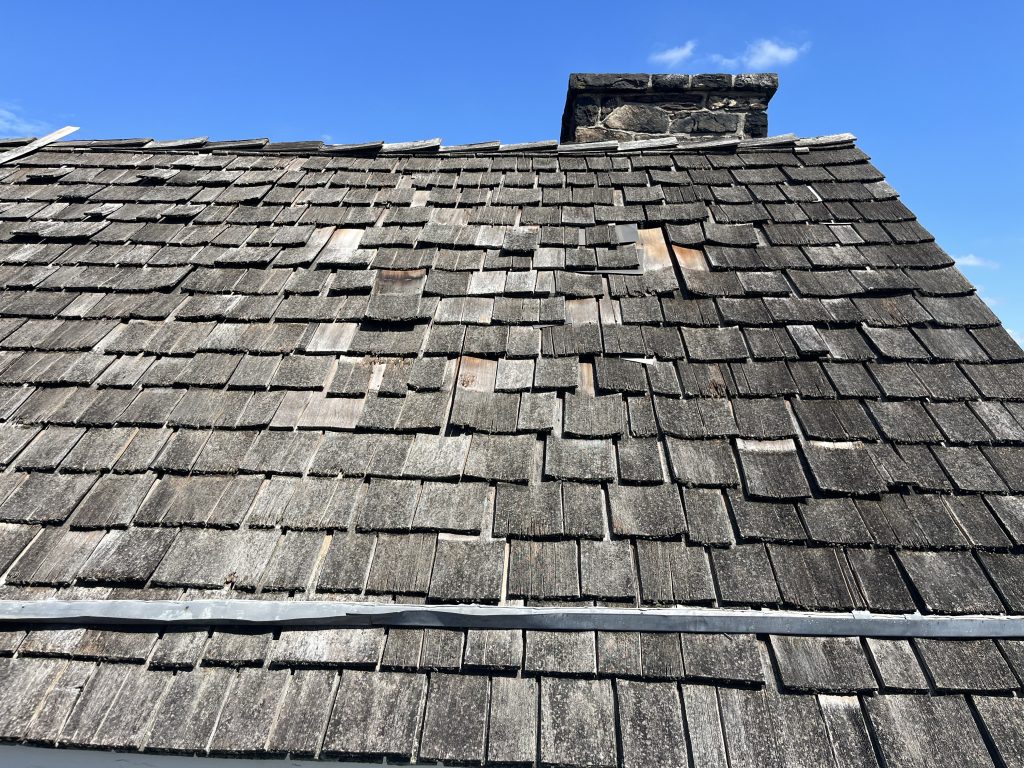 Worn cedar shake roof with visible damage and deterioration on a commercial building before restoration.