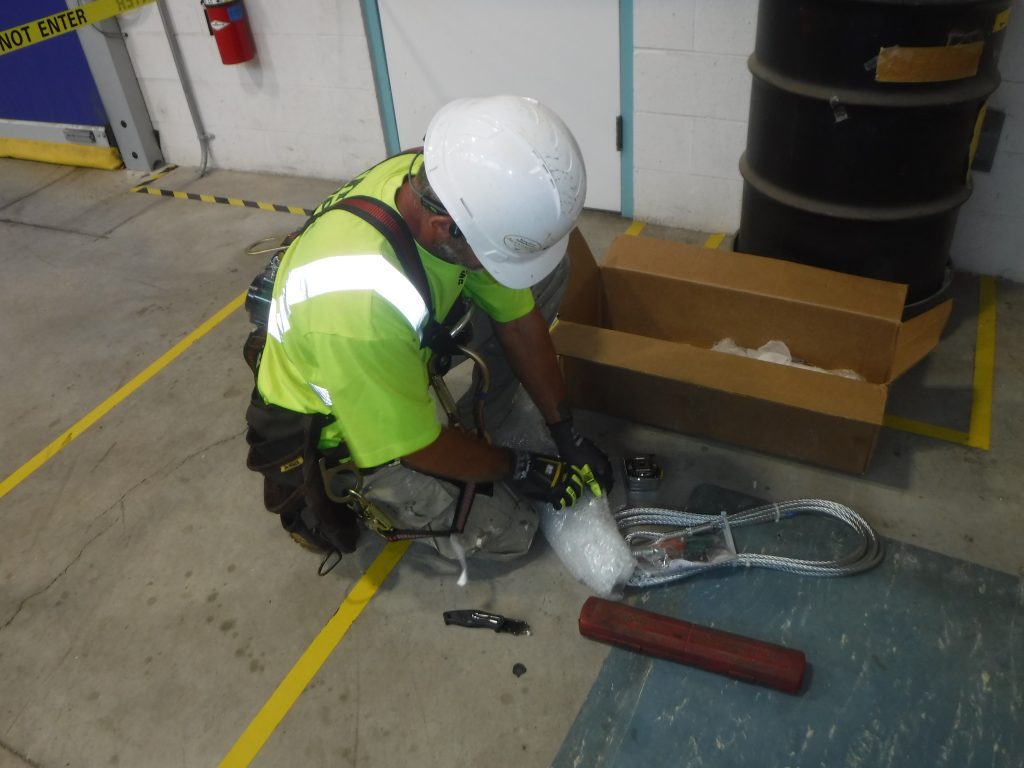 GSM Roofing technician unpacks and inspects stainless steel cable for fall protection installation at TE Connectivity.