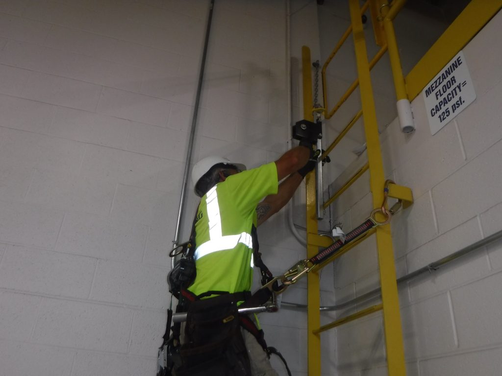 Technician using safety gear while mounting the vertical cable for the ladder climb system on an interior dock ladder.