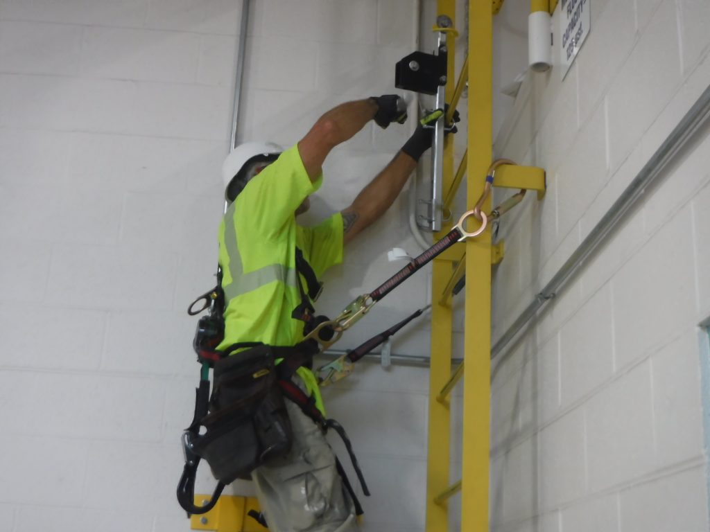 GSM Roofing technician wearing full fall protection gear while securing hardware for the ladder safety system installation.