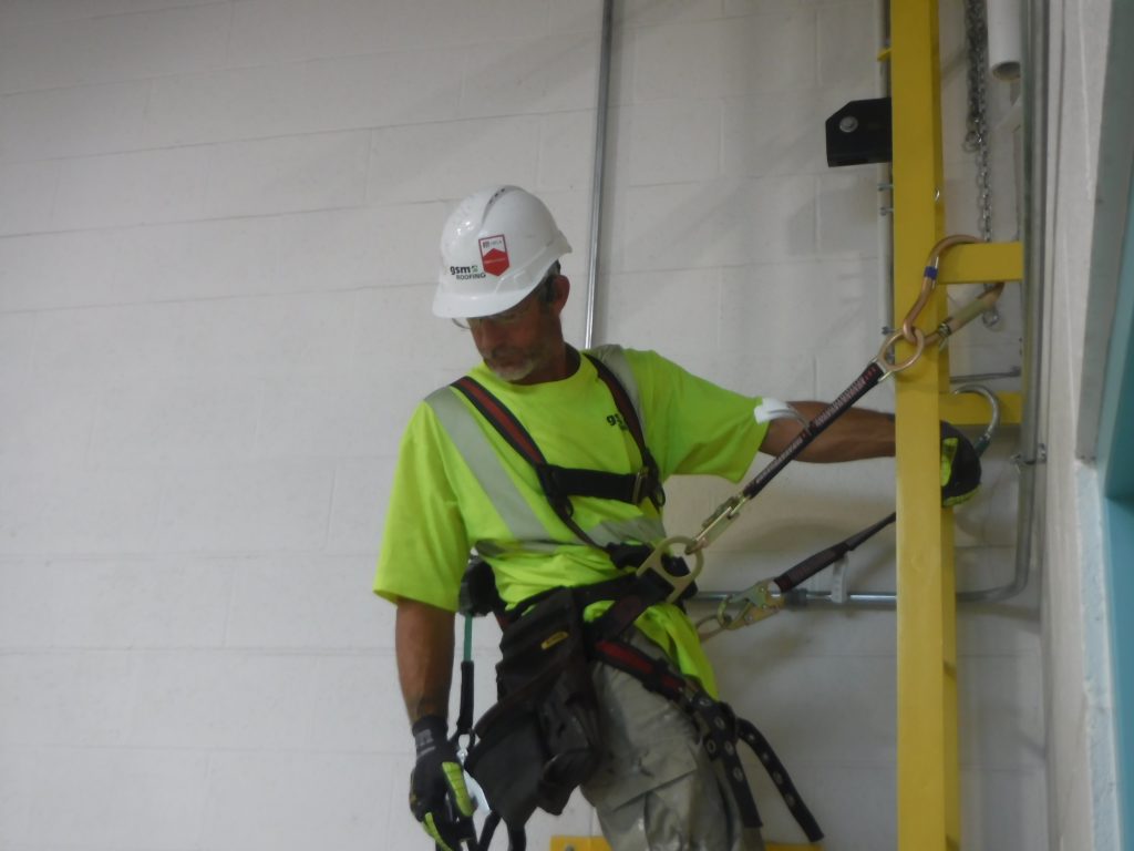 Close-up of a GSM Roofing technician inspecting and adjusting fall arrest connection points during system installation.