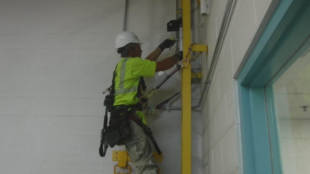 GSM Roofing technician installing the top bracket of the Safewaze ladder fall protection system while securely harnessed.