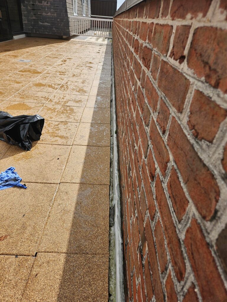 Close-up view of rubber paver installation showing edge alignment and drainage clearance next to a red brick parapet wall.