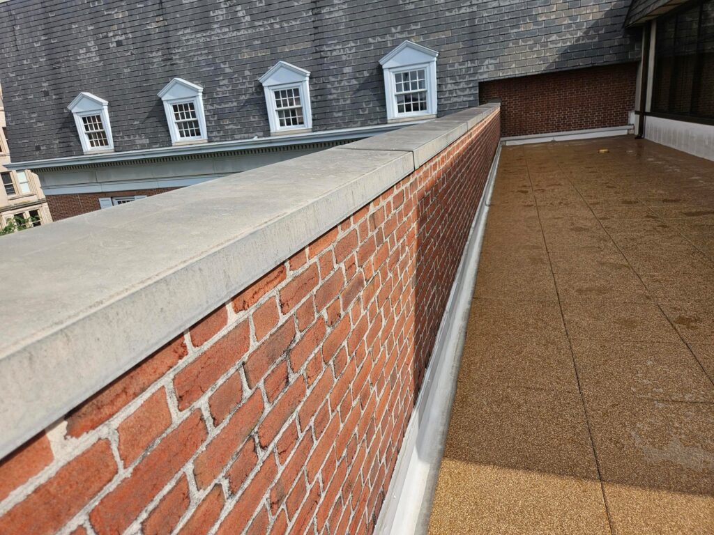 Clean alignment of interlocking rubber rooftop tiles next to historic brick parapet and slate-roofed building.