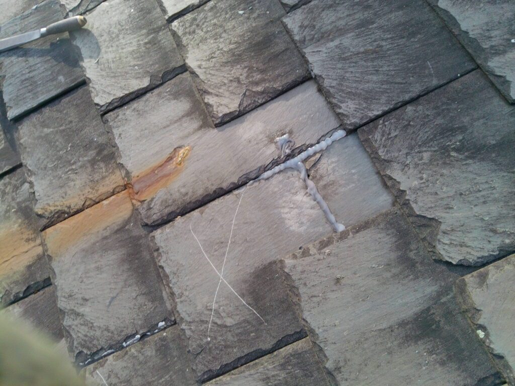 Silicone caulk applied across cracked natural slate joints on historic church roof in Tyrone PA Blair County documented by GSM Roofing during initial assessment showing improper prior repair method 2024